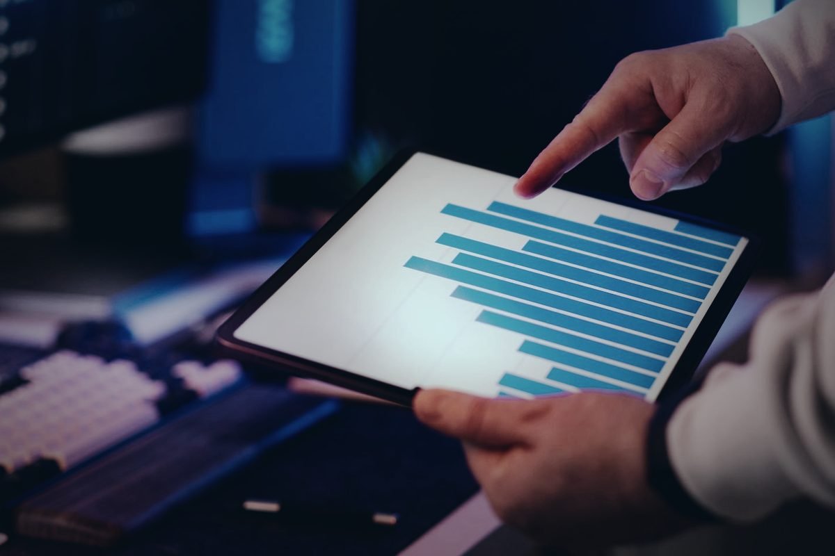 Mano señalando una gráfica de barras azul en la pantalla de una tableta